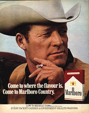 Close-up of Roy in cowboy hat lighting a cigarette, from a Marlboro print ad.