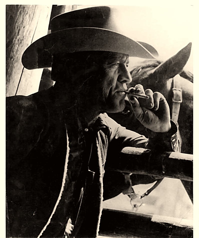 Roy N. Sickner in profile, lighting a cigarette beside a saddle horse, in a fleece-lined coat and cowboy hat — black-and-white portrait from his Marlboro years, 1960s–1970s.